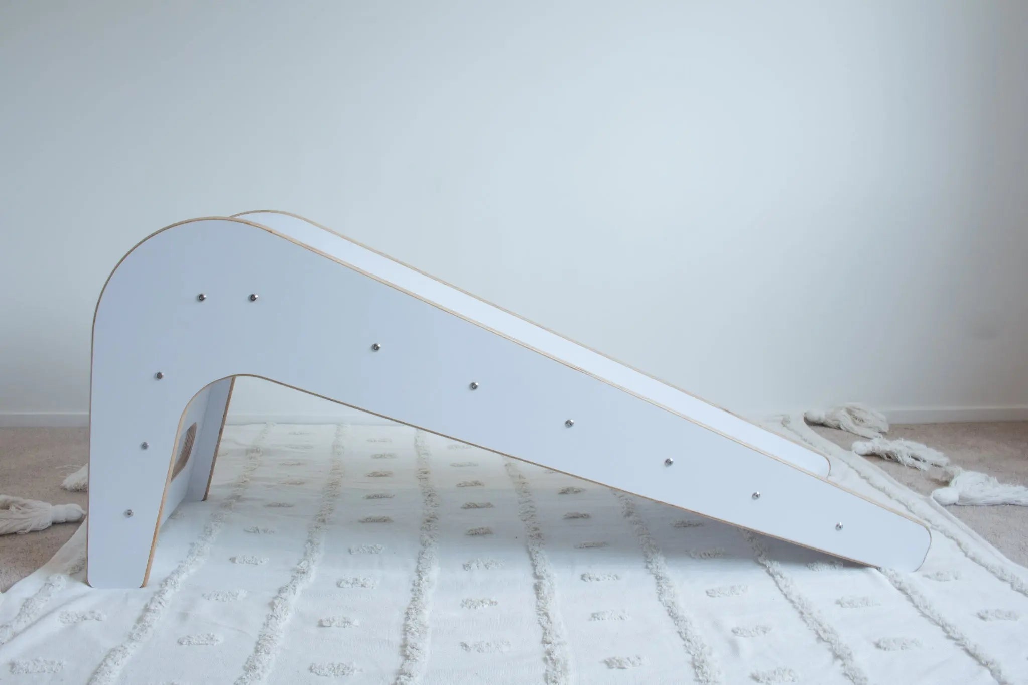 A wooden, white slide shown side on sitting on top of a white tufted rug