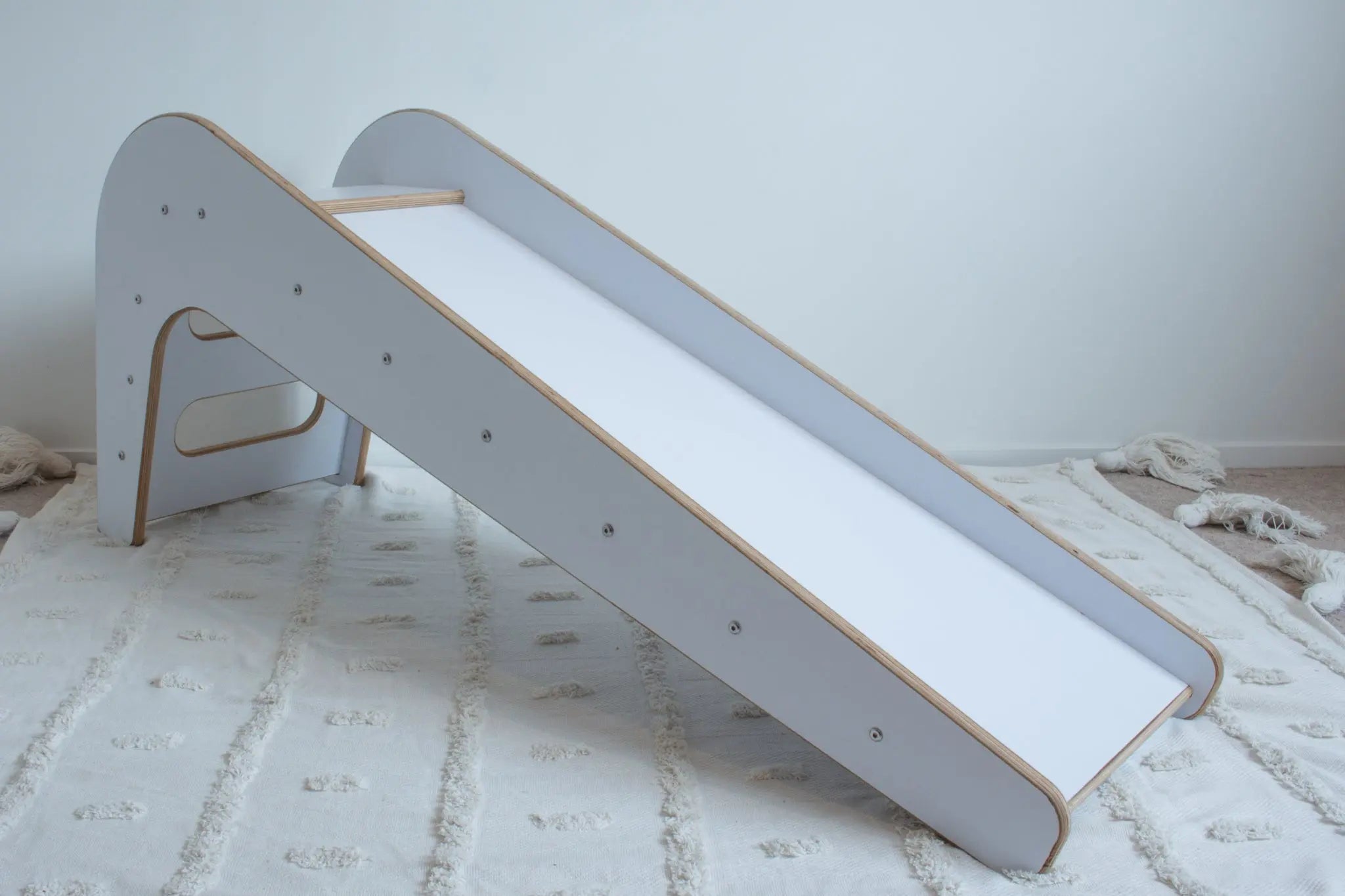 A wooden, white slide shown from its front-left side sitting on top of a white tufted rug