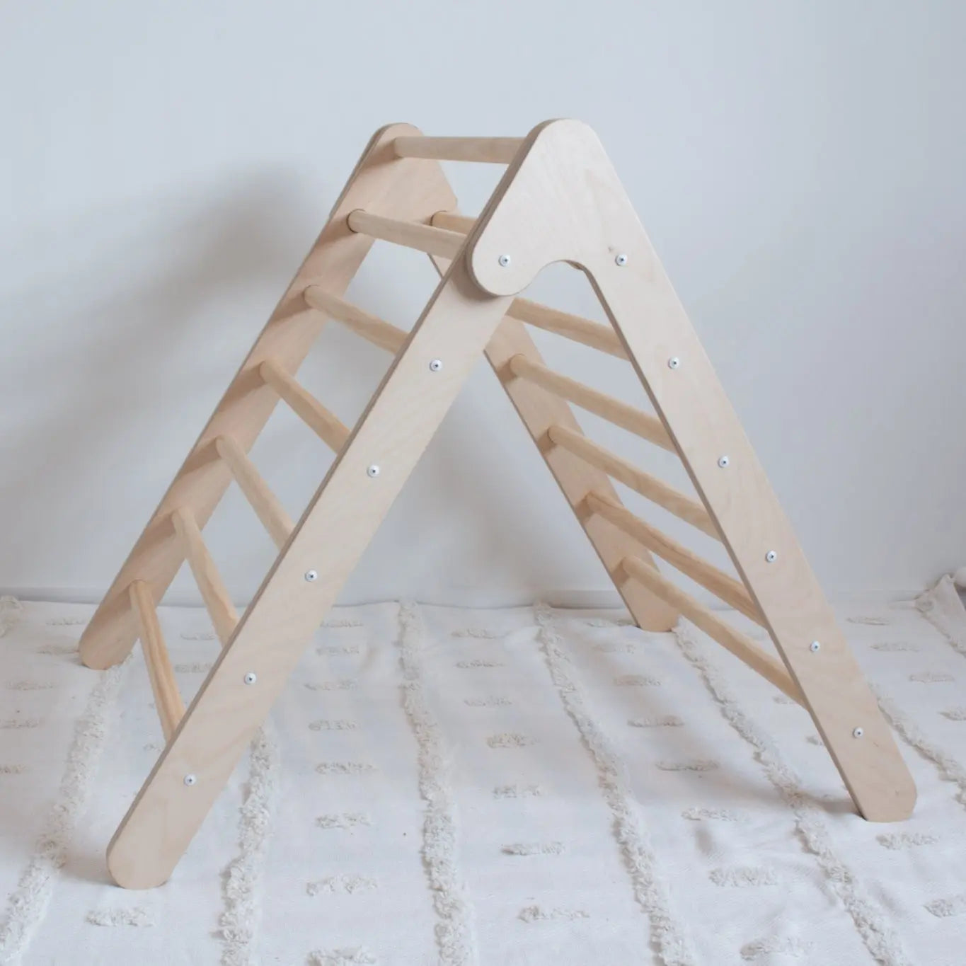 A side on view of a wooden foldable climbing frame on top of a rug