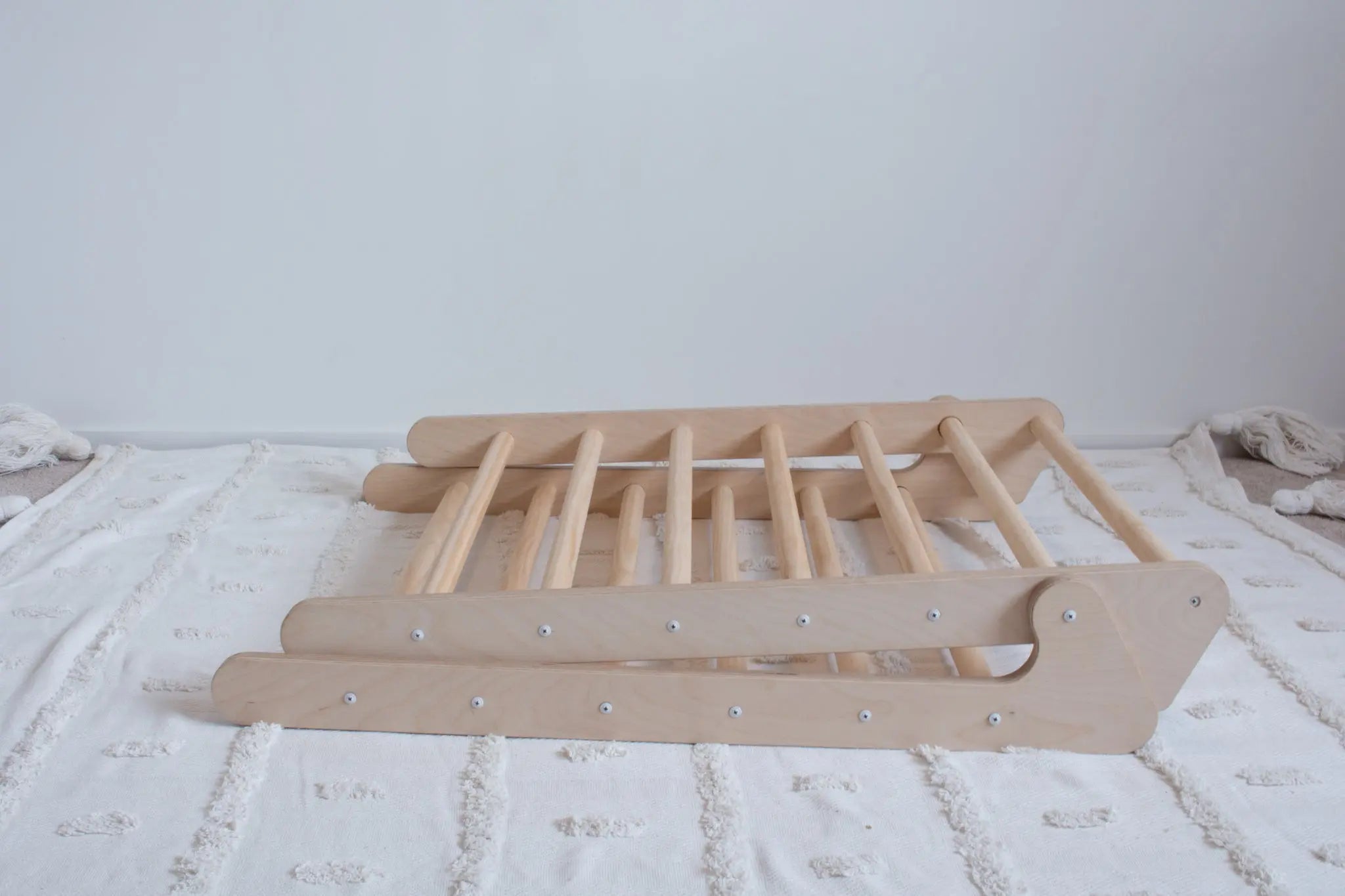 A wooden foldable climbing frame lying folded up on top of a rug