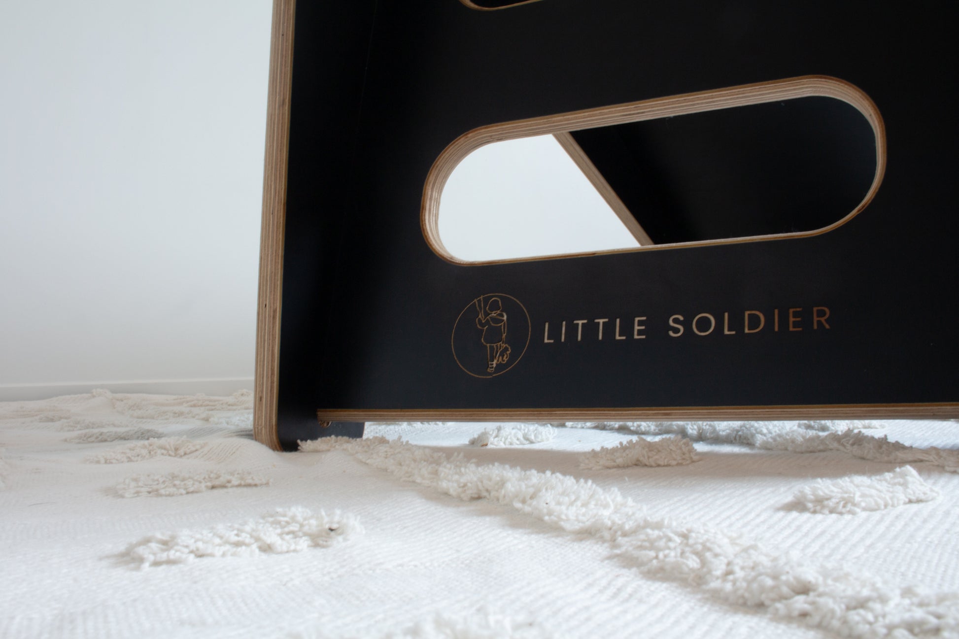 A close up image of the Little Soldier logo on the steps of a black wooden slide.