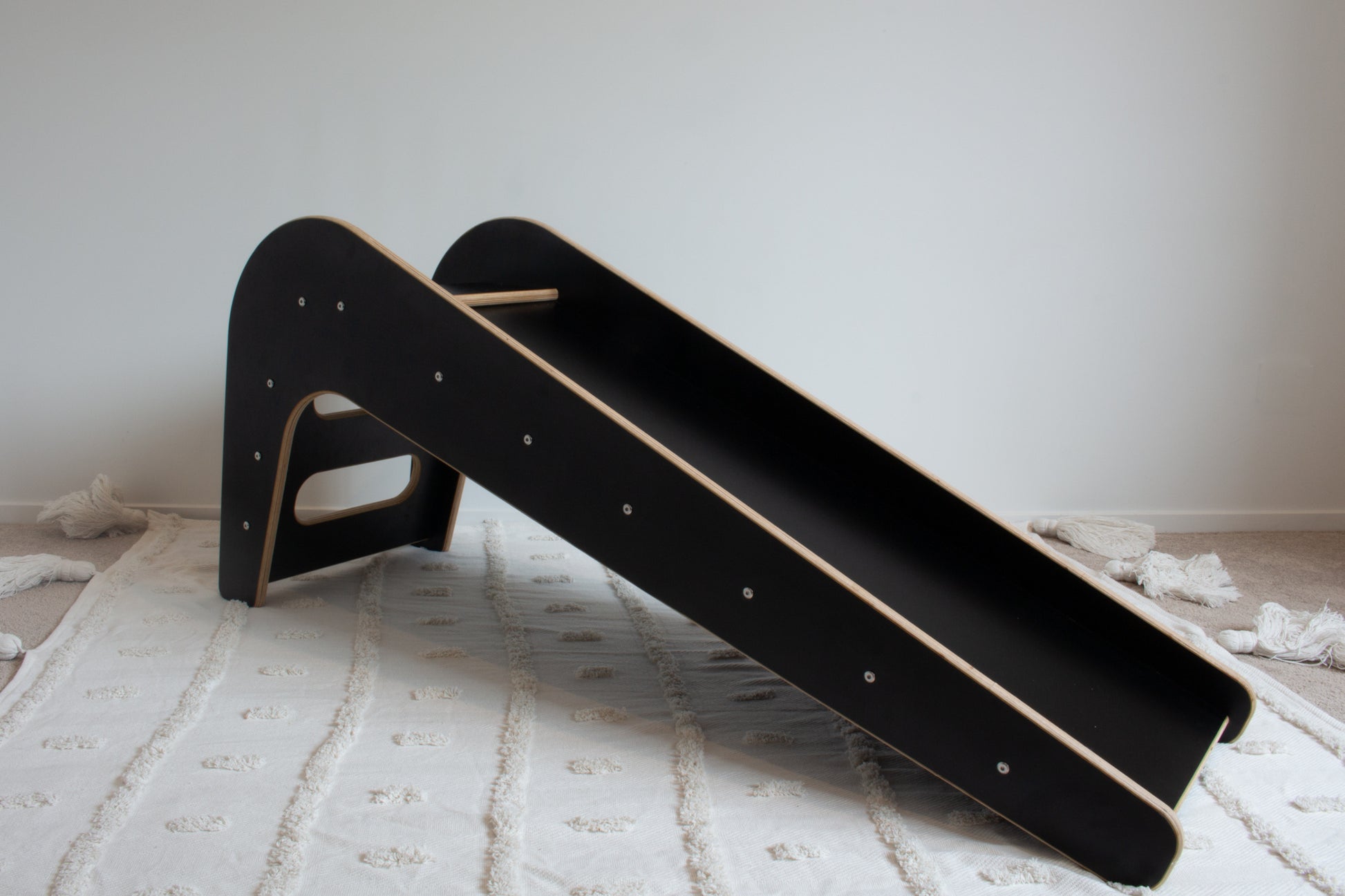 A wooden, black slide shown from its front-left side sitting on top of a white tufted rug