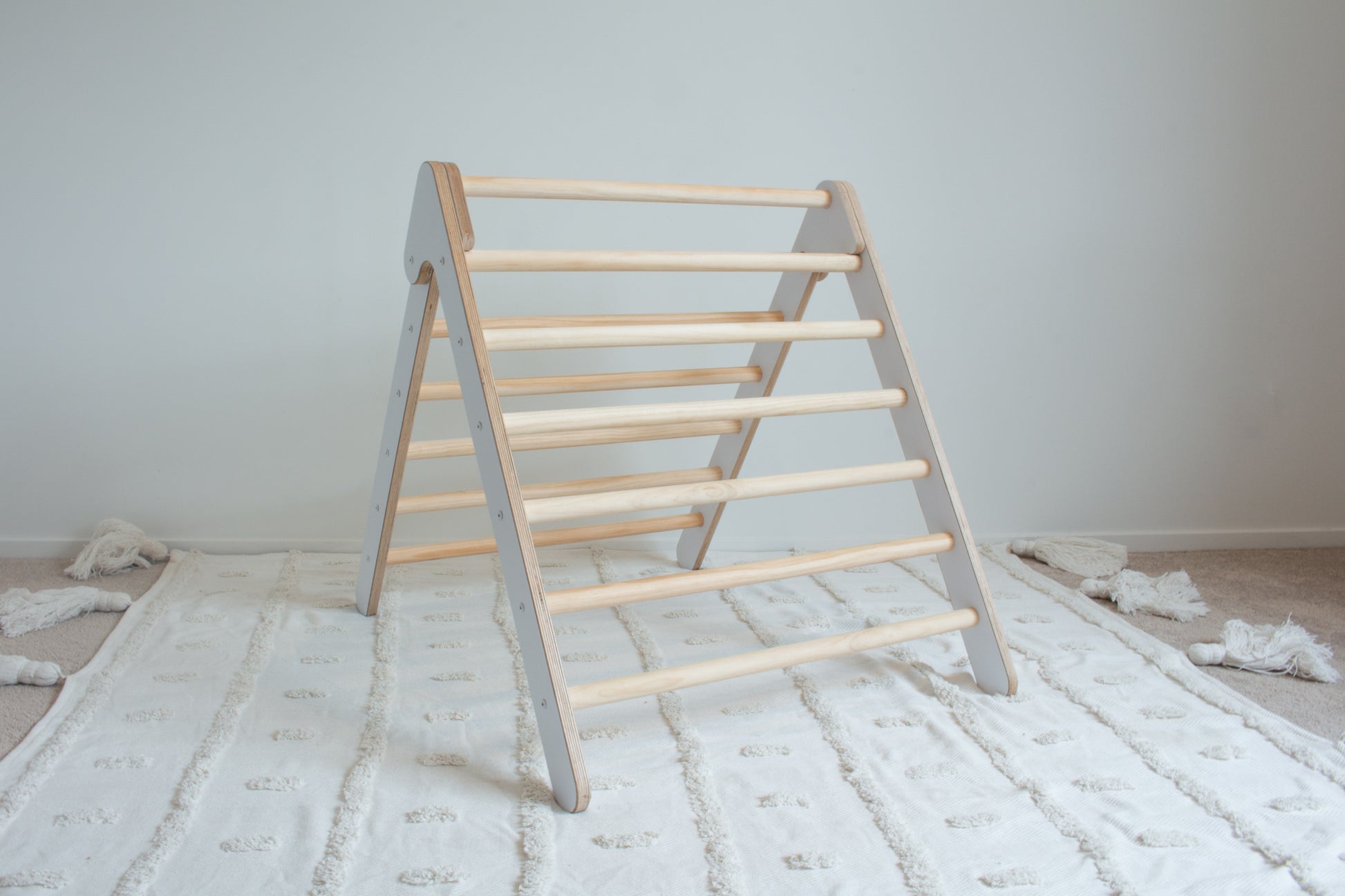 A white, foldable climbing frame sitting open on top of a tufted white rug