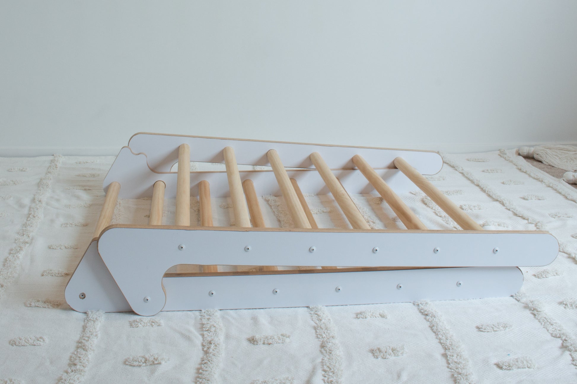 A white climbing frame folded up and lying down on a rug