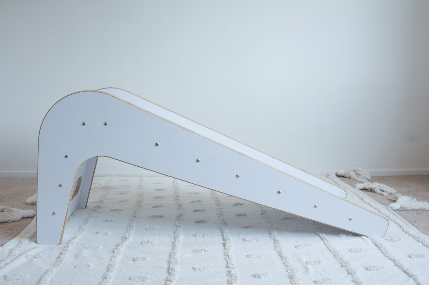 A wooden, white slide shown side on  sitting on top of a white tufted rug