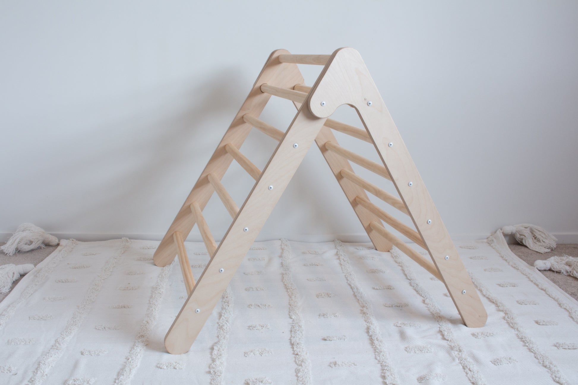 A side on view of a wooden foldable climbing frame on top of a rug