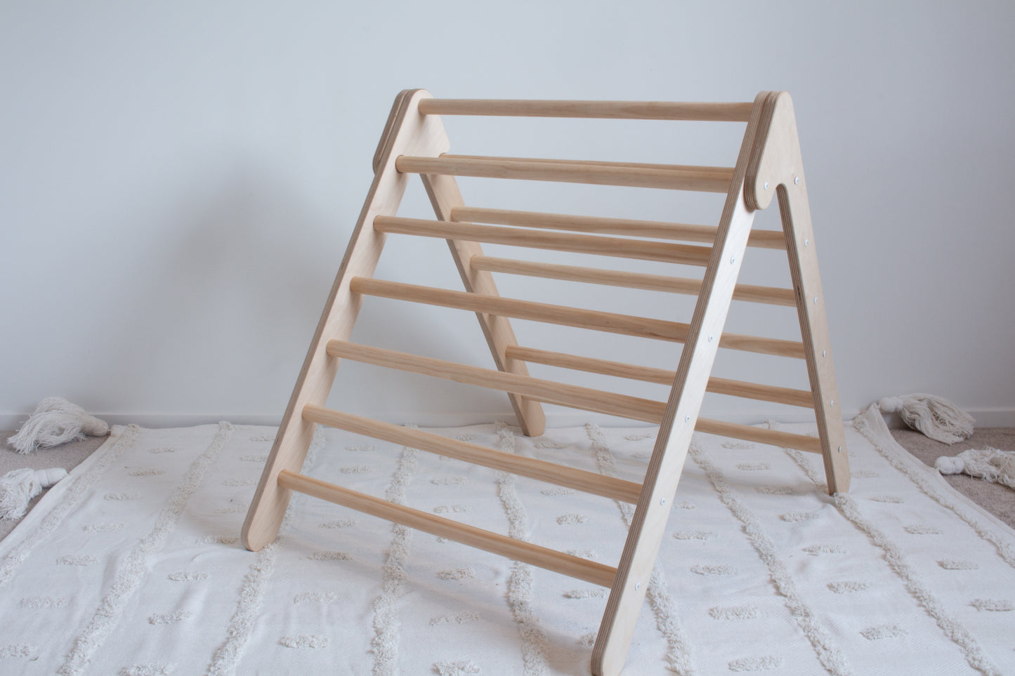 A wooden, foldable climbing frame sitting open on top of a tufted rug