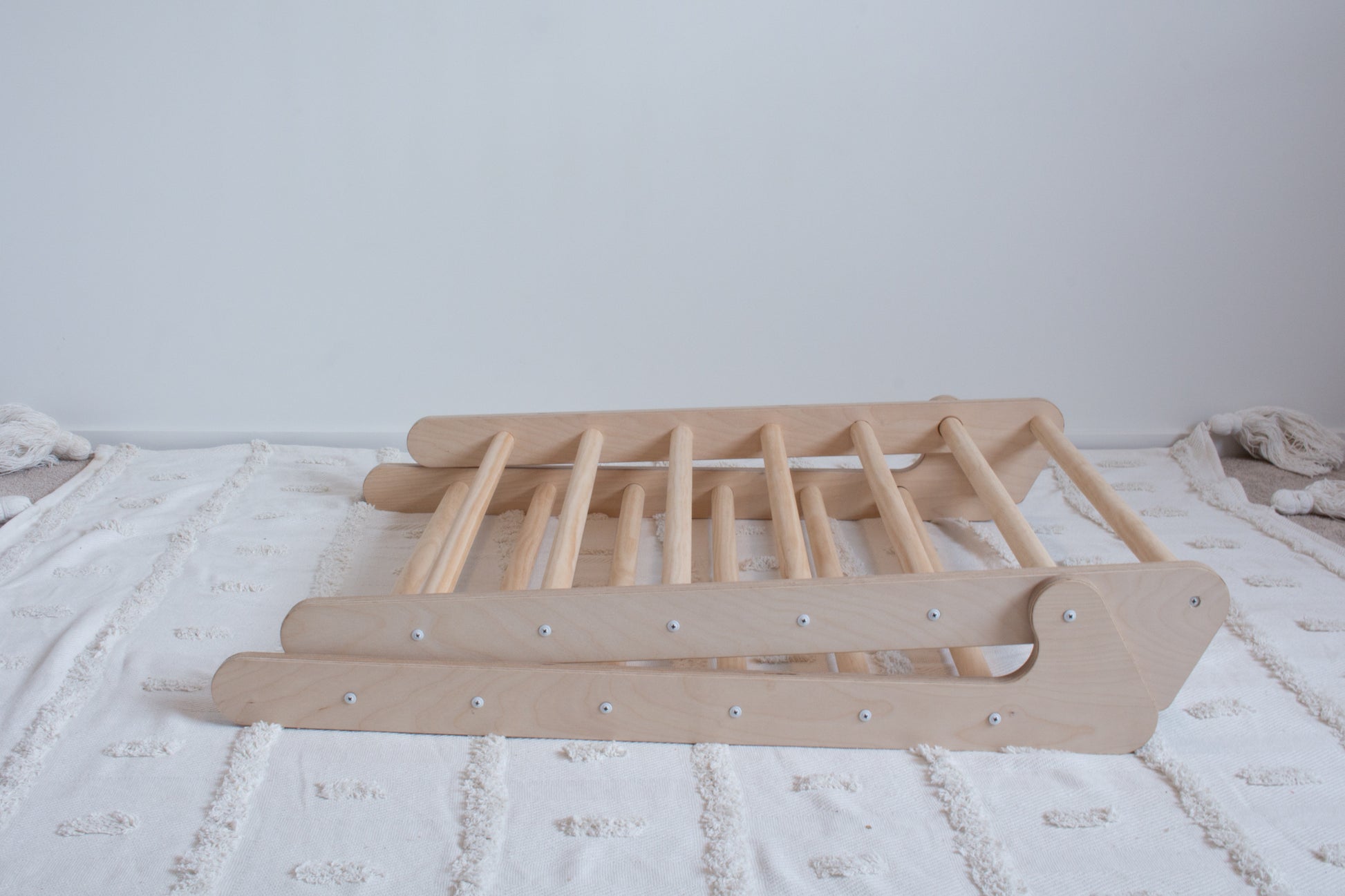 A wooden foldable climbing frame lying folded up on top of a rug