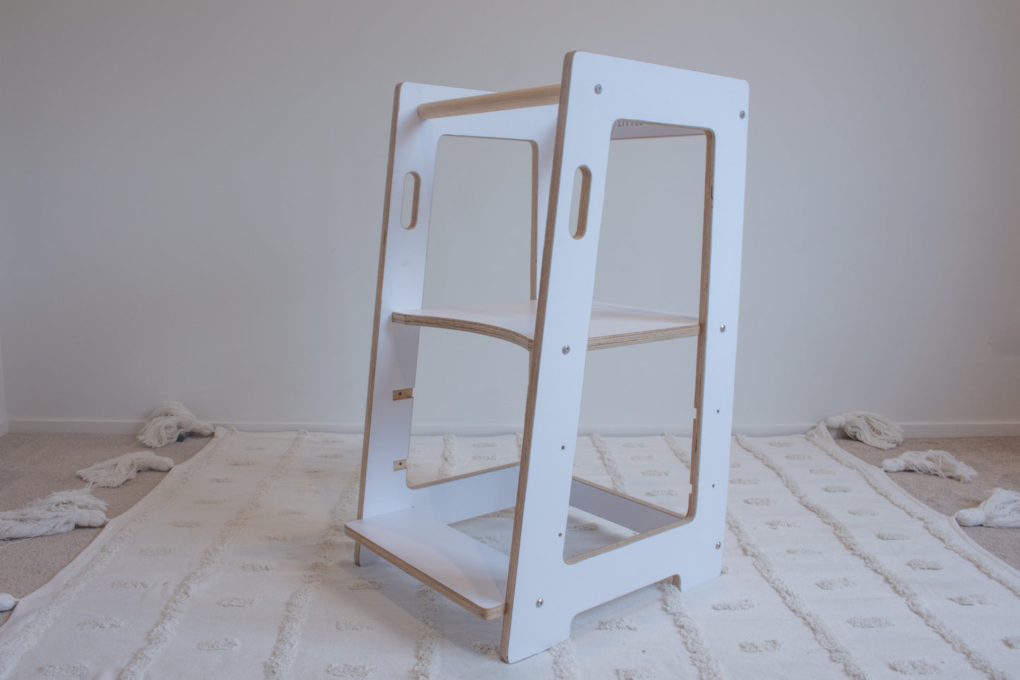 A white kitchen helper viewed from the right-front side sitting on top of a tufted rug. The adjustable platform is set to the highest setting.